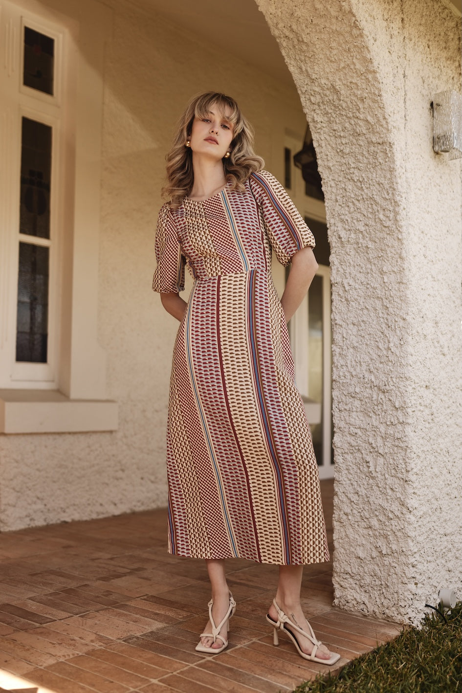Woman in a patterned dress standing in front of a stone building.