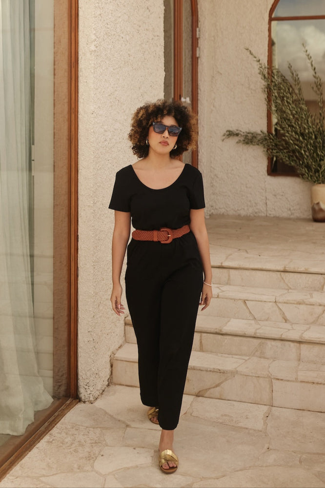 
                      
                        Woman in a black outfit with a tan belt standing on stone steps.
                      
                    