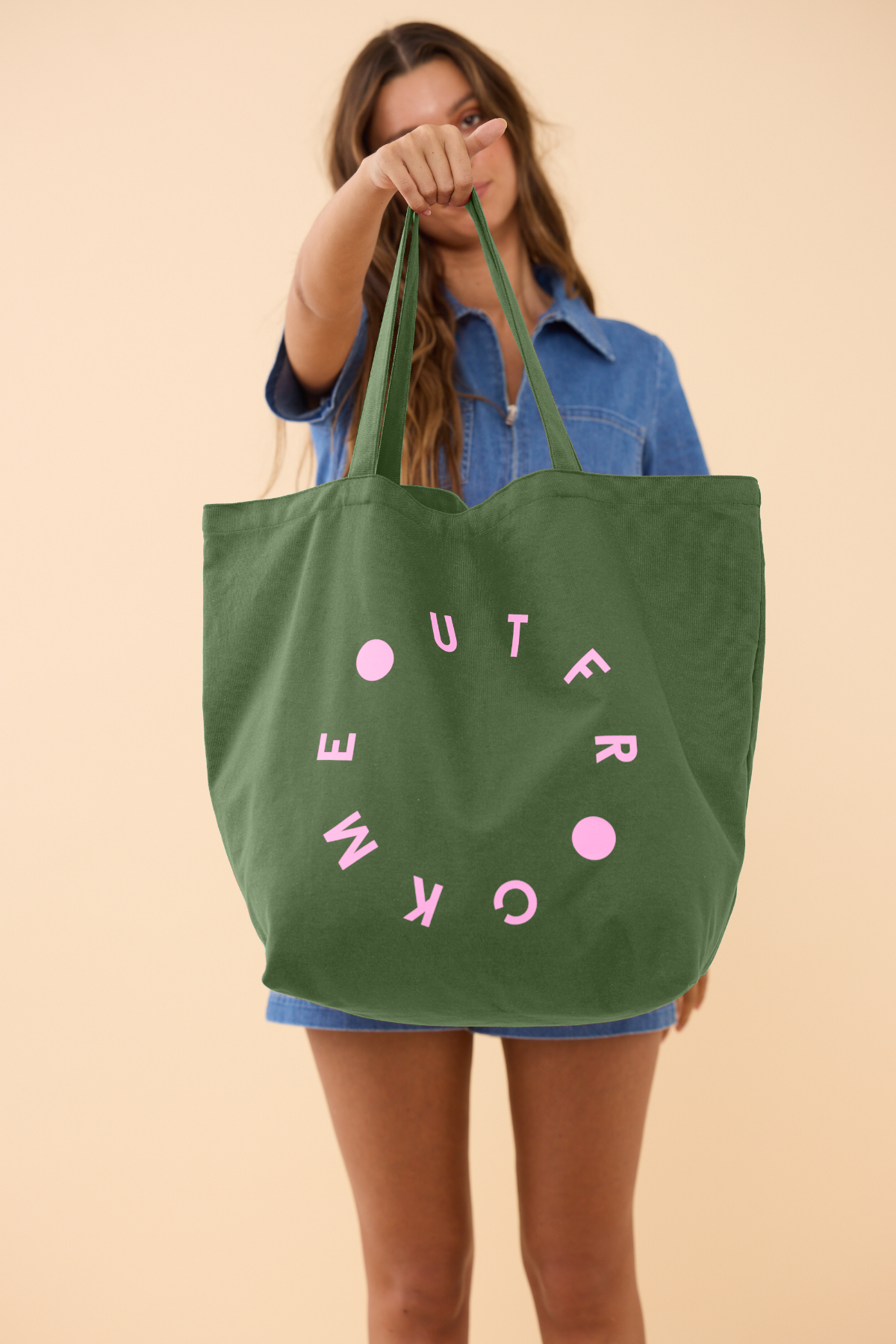 Person holding a green tote bag with pink text against a beige background
