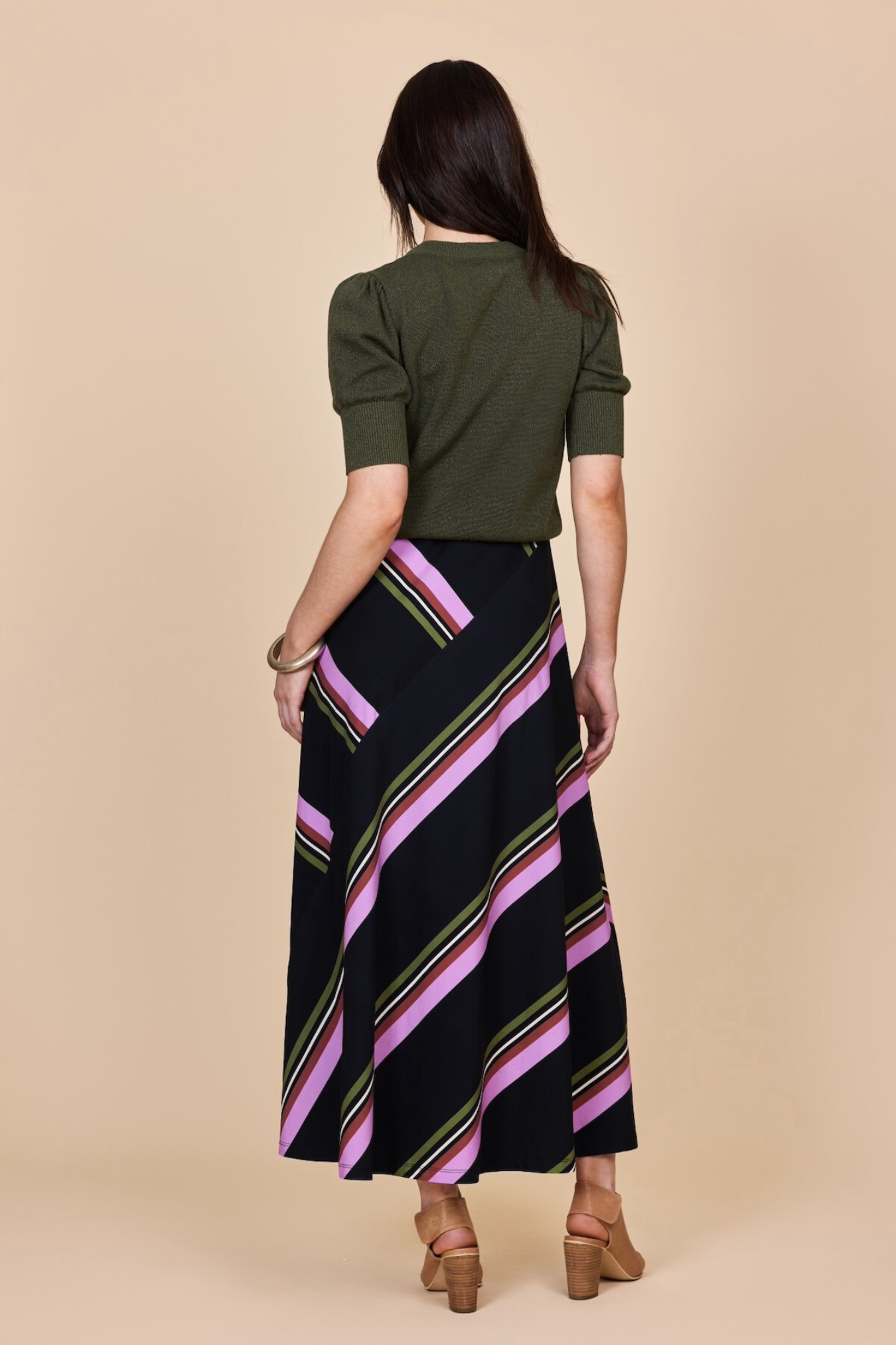 Woman wearing a green top and black striped skirt on a beige background