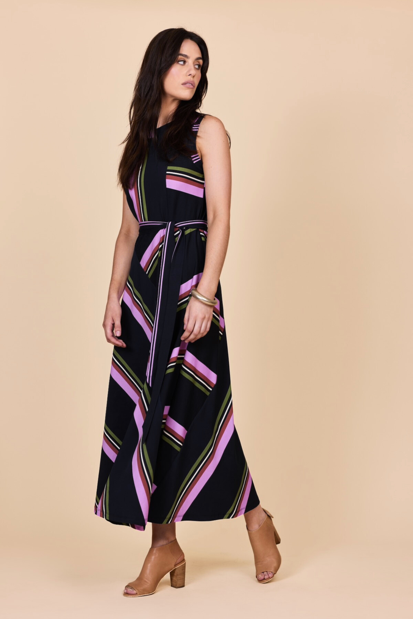 Woman wearing a black sleeveless dress with Olive green and orchid stripes on a beige background