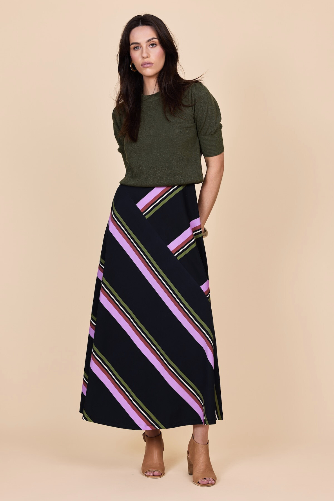 Woman wearing a green top and black striped skirt on a beige background