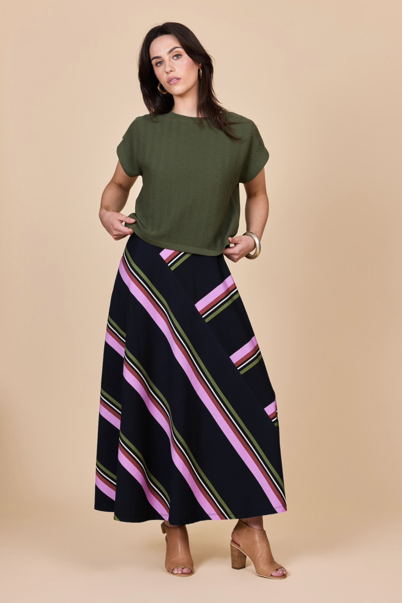 Woman wearing an olive green top and black striped skirt on a beige background