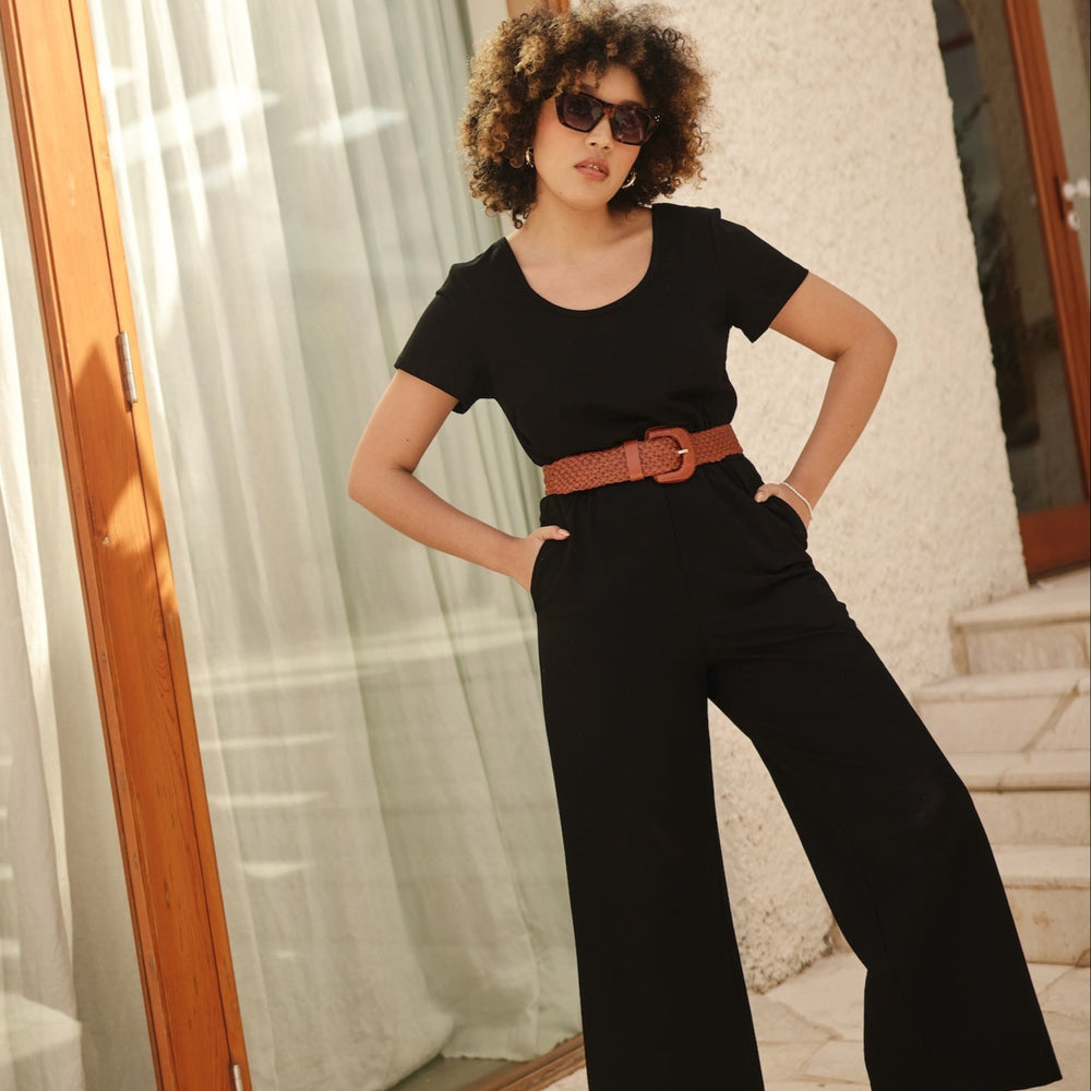Woman in a black outfit with a tan belt standing in front of a glass door.