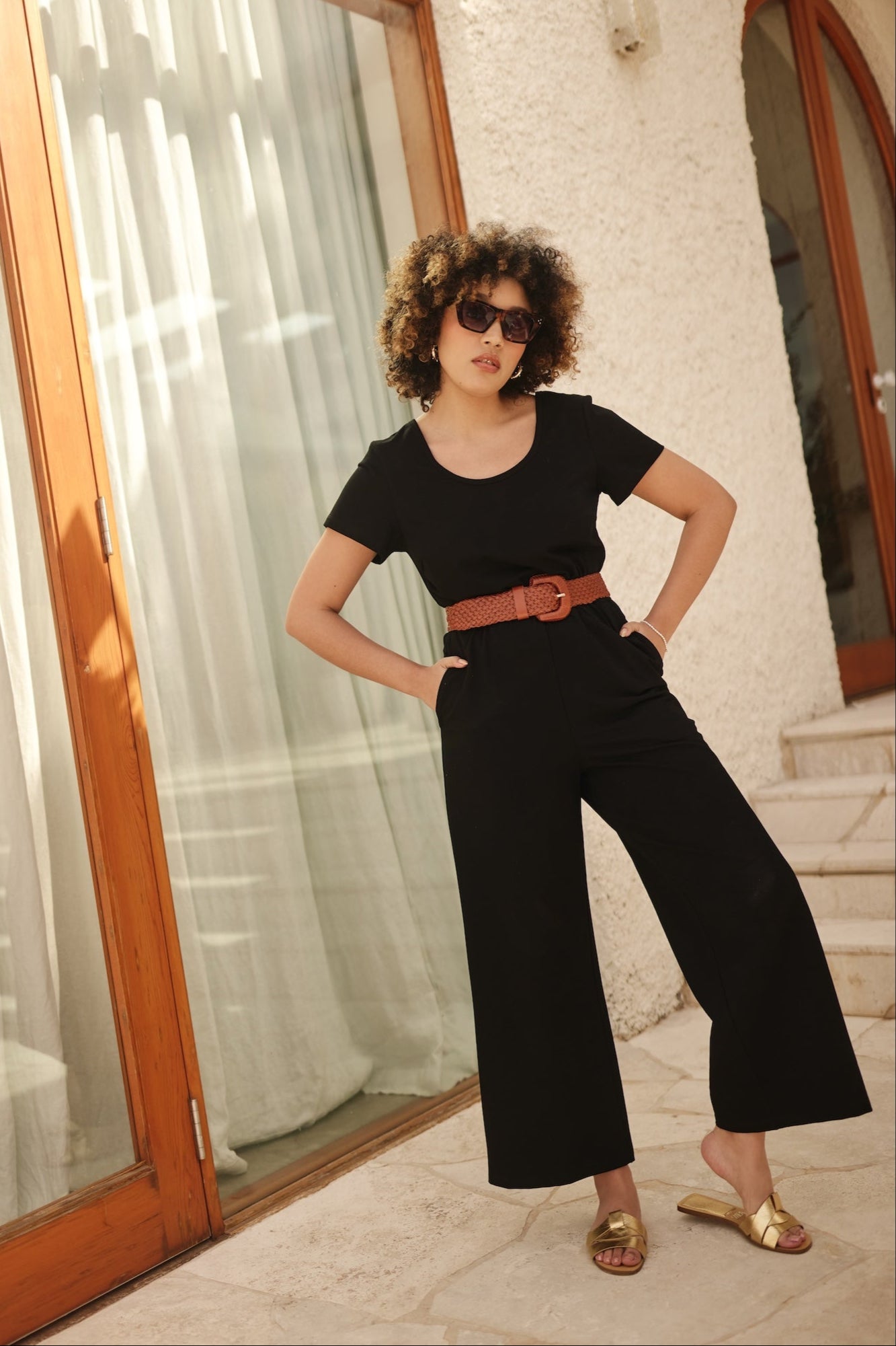 Woman in a black outfit with a tan belt standing in front of a glass door.