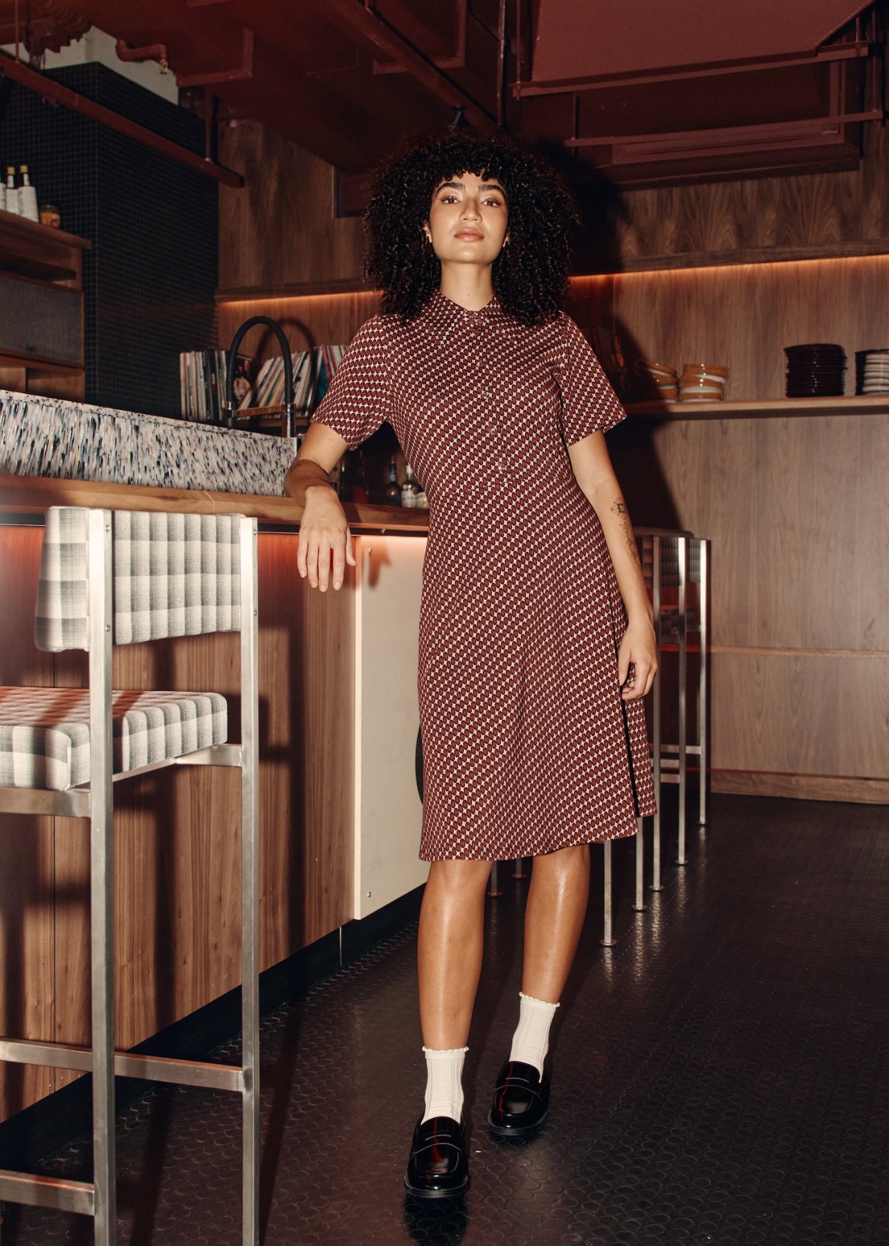 Woman in a retro patterned dress standing in a bar setting