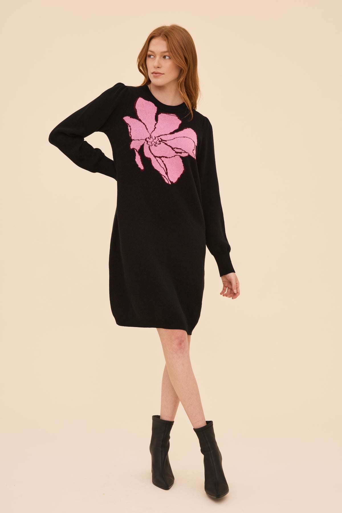 Woman wearing a black knitted dress with a pink magnolia design on a beige background