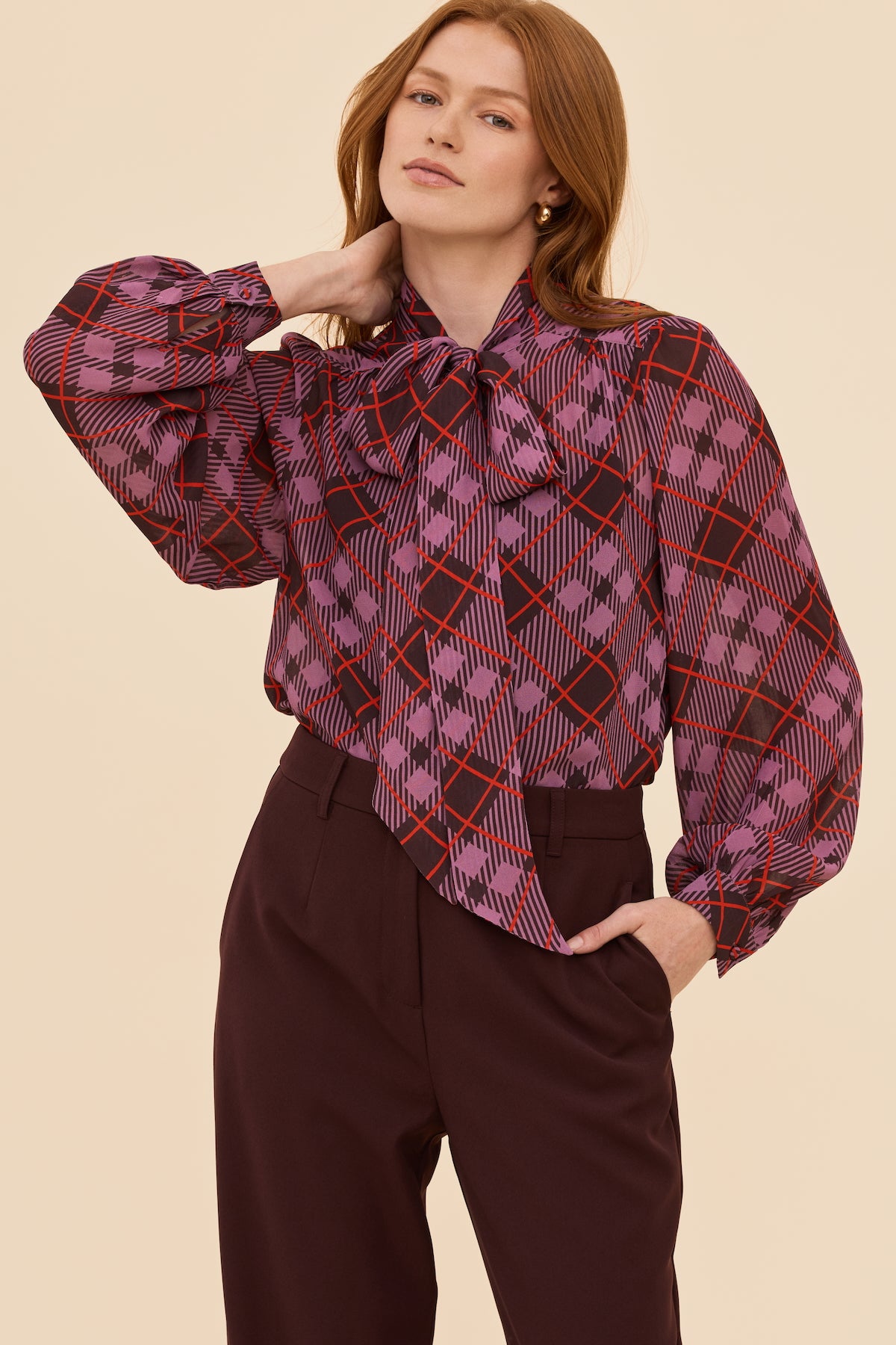 Woman wearing a plaid blouse with a bow tie on a beige background