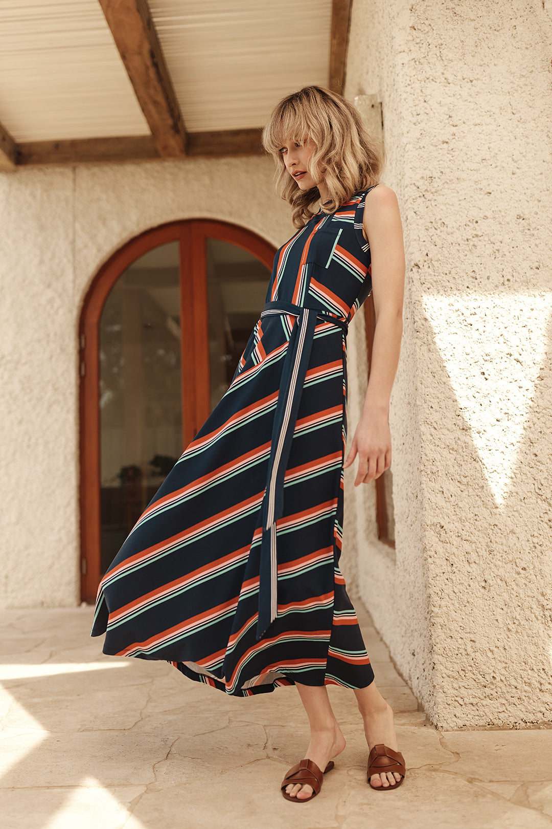 Woman wearing a striped dress standing against a textured wall.